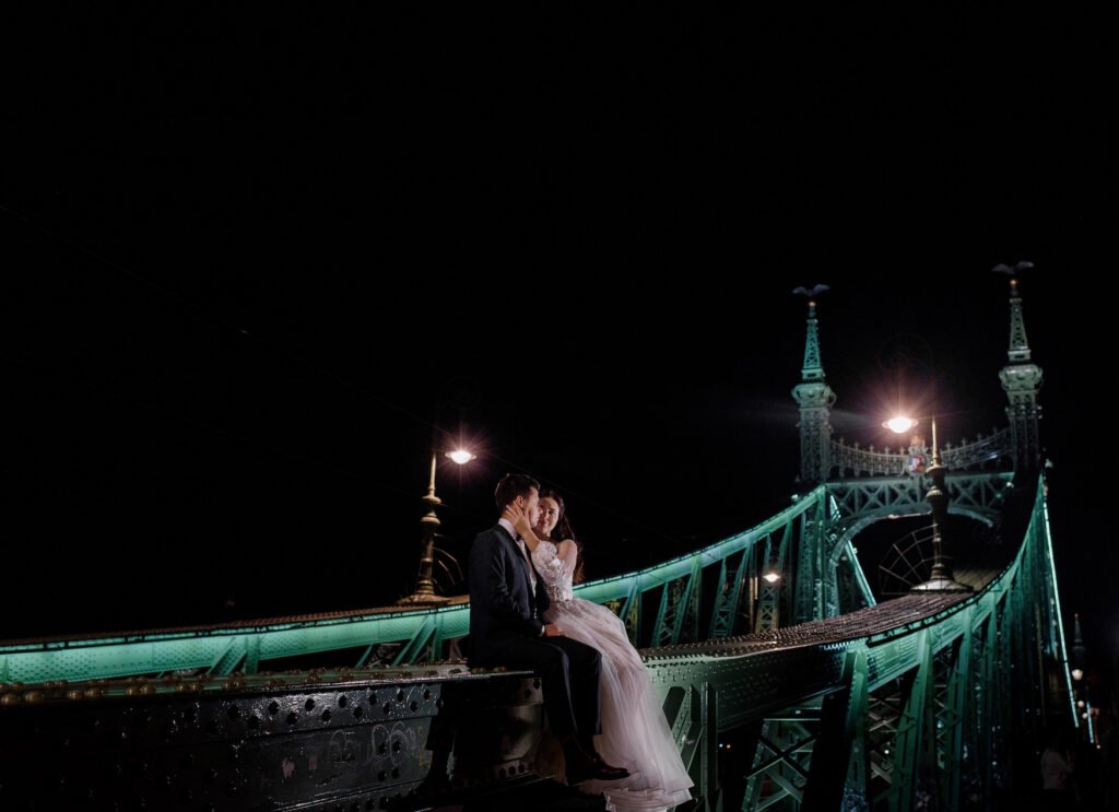 Romantic wedding couple sitting on an illuminated bridge in London at night
